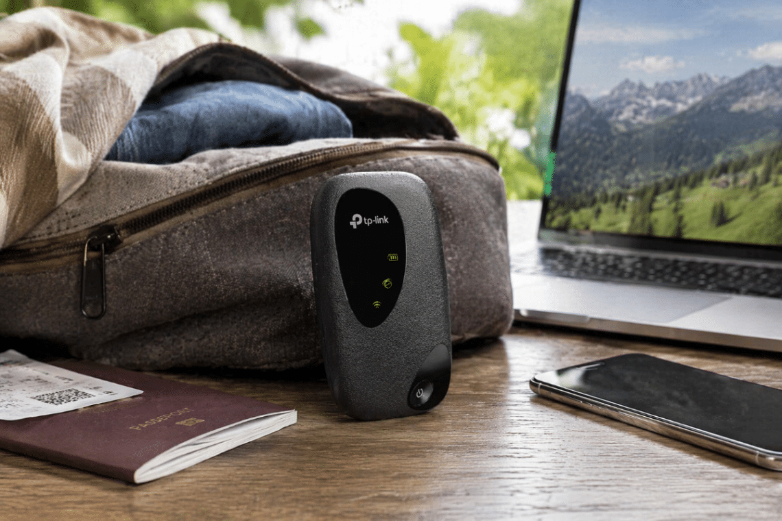 Routeur mobile TP-Link M7000 posé sur une table à côté d’un ordinateur portable, d’un smartphone et d’un sac de voyage